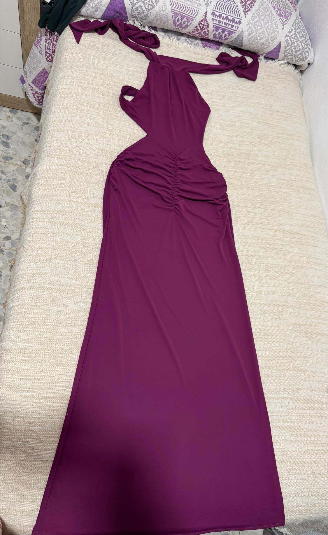 Purple maxi dress with a halter neck, cut-outs, and ruched detailing, laid out on a bed with a beige bedspread and patterned cushions.