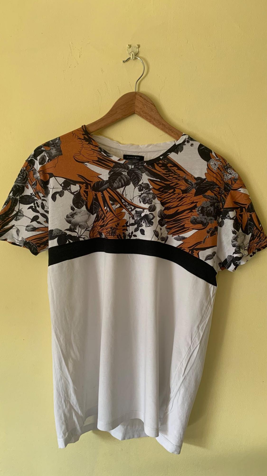 Front view of white t-shirt with orange and black floral print on the chest.
