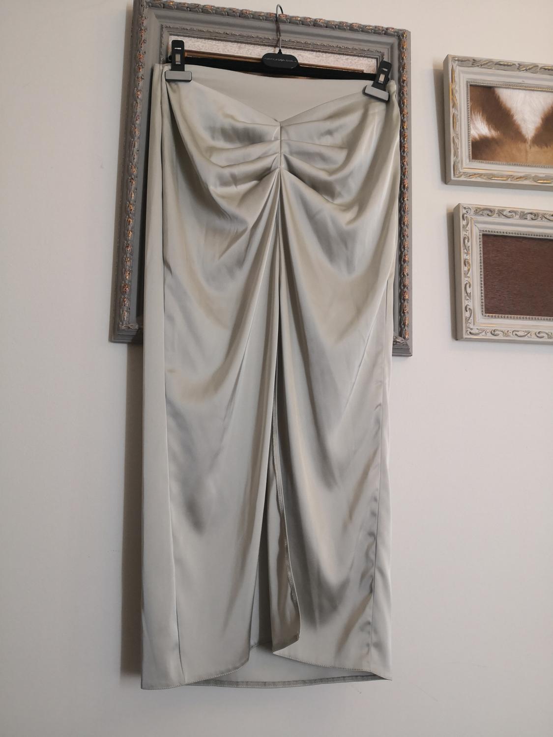 A light grey pleated maxi skirt hanging in a decorative frame, with small pictures on the wall in the background.