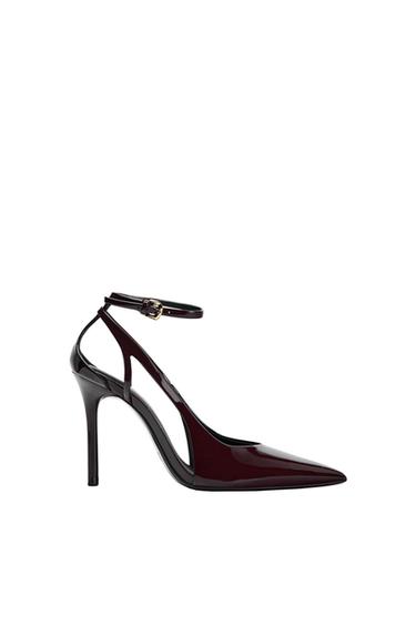 High-heeled shoe in burgundy patent leather with a pointed toe and adjustable ankle strap on a white background.