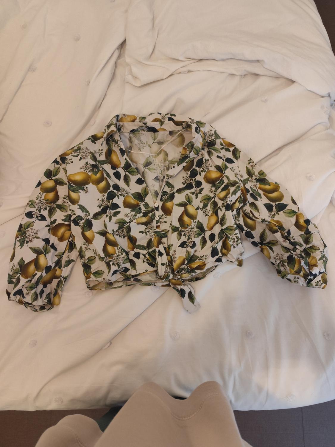 Long-sleeved blouse with lemon and leaf print on a bed with white sheets.