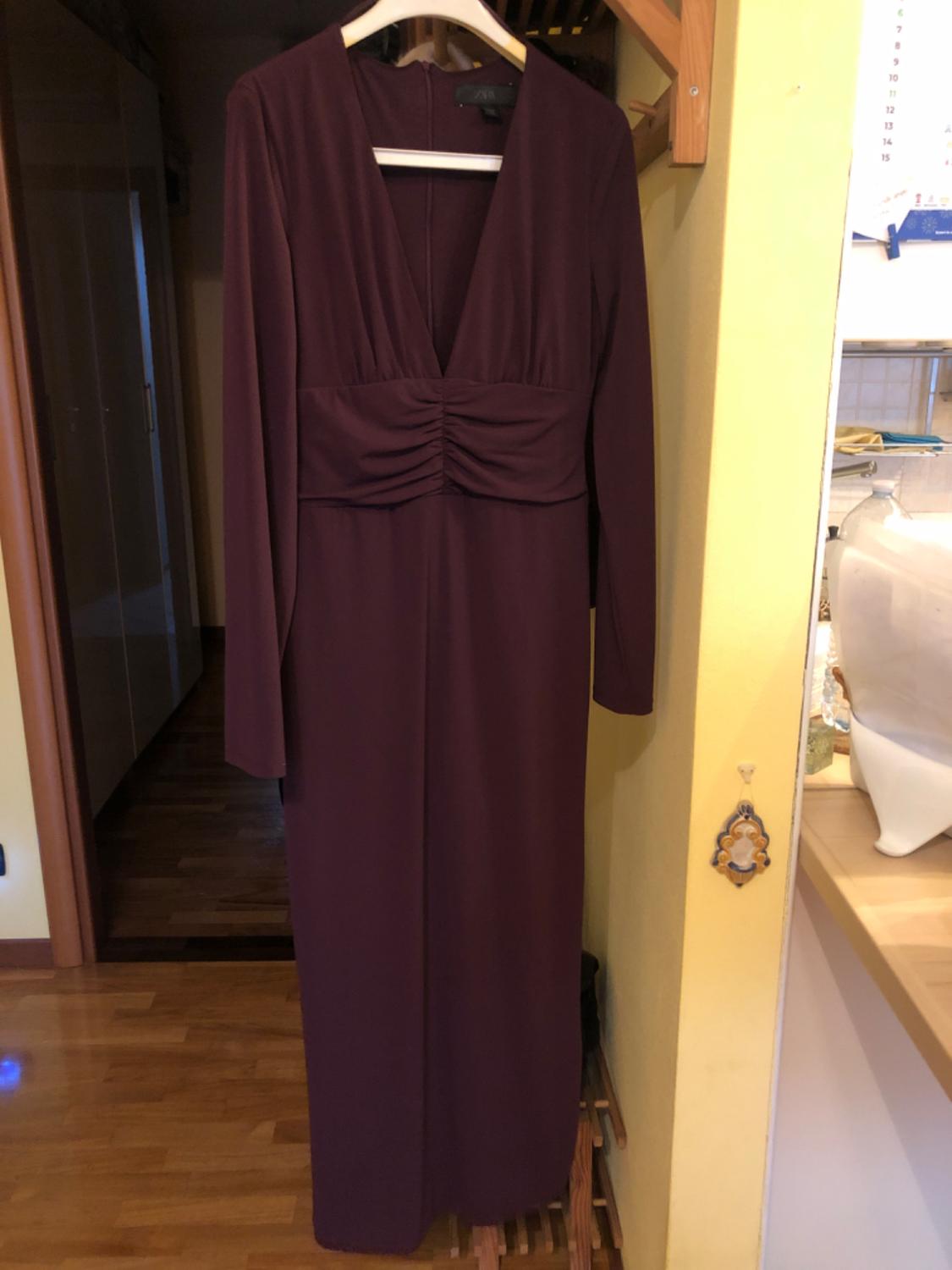 Burgundy long dress with a V-neckline and long sleeves, hanging on a hanger indoors with a wooden floor.