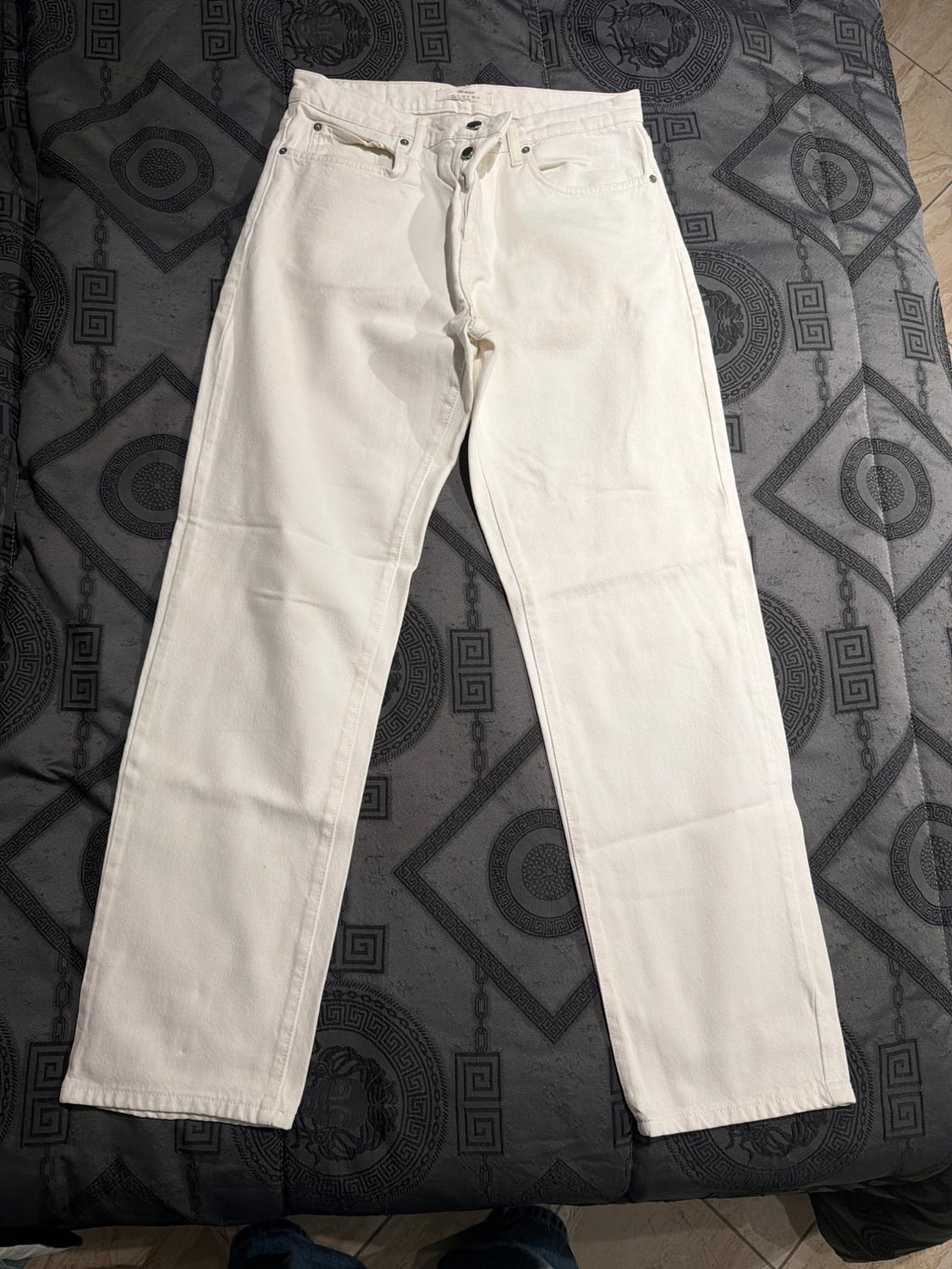 White denim trousers laid out on a grey bedspread with geometric patterns and circular details.