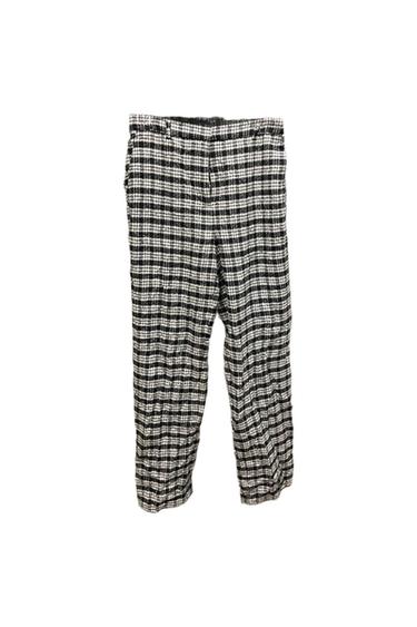 Black and white plaid pants, hanging on a white background. Classic and relaxed design, ideal for a casual look.