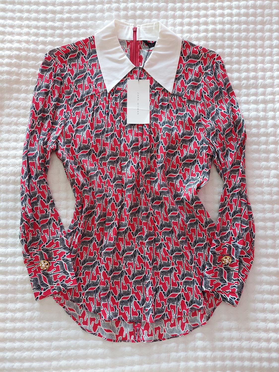 Red long-sleeved blouse with zebra print, white collar, and ZARA WOMAN label on a textured white background.