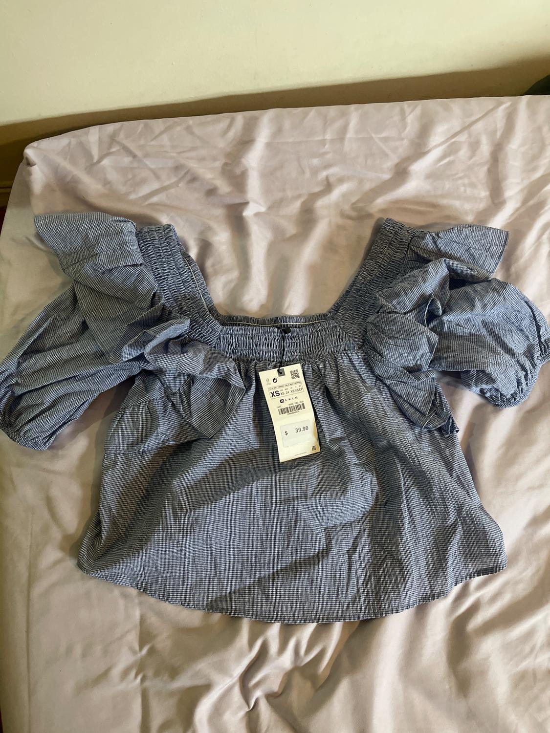 Blue blouse with puff sleeves on a bed. Visible tag with size XS and price $39.90. Wrinkled fabric.