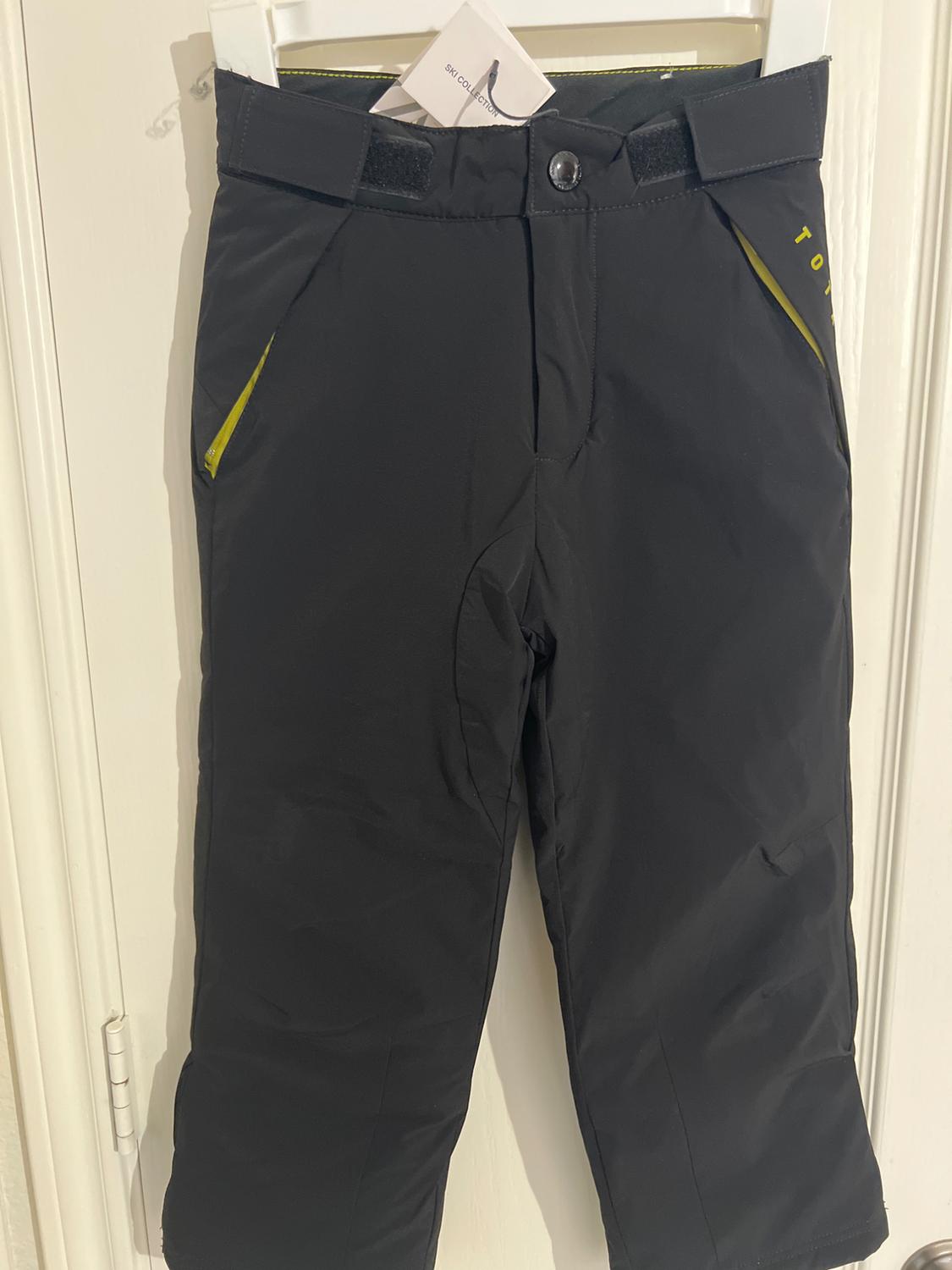 Black ski pants hanging on a white hanger, with yellow details on the pockets and a tag that says "SKI COLLECTION."