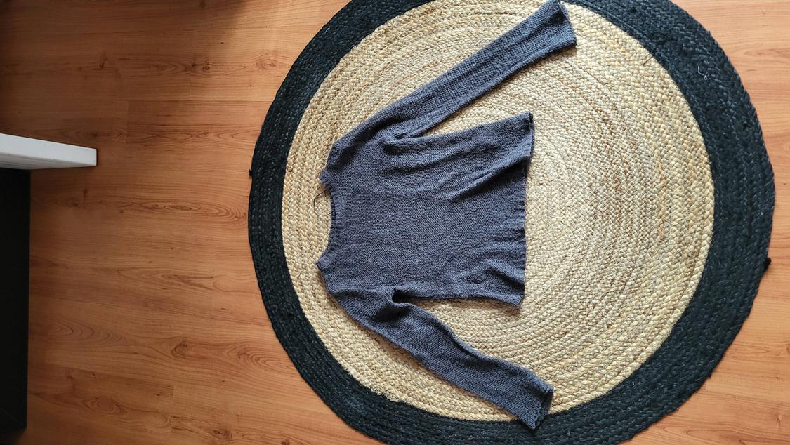 Grey long-sleeved jumper on a round jute rug on a light wooden floor.