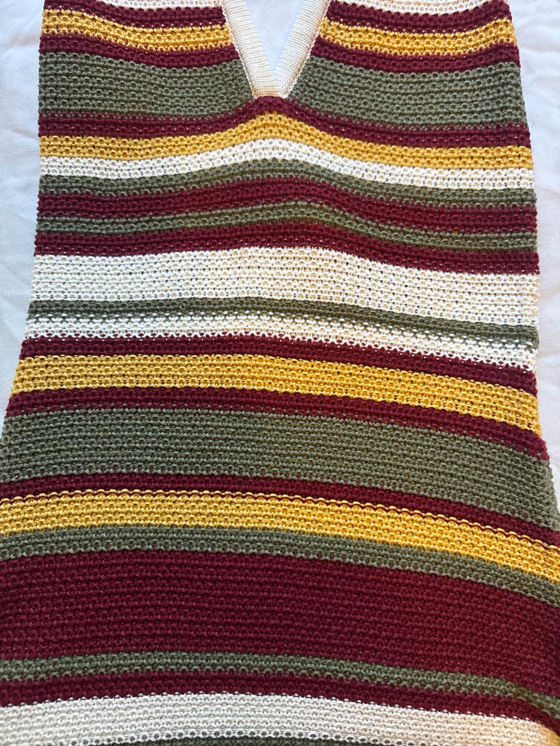 Knitwear detail with a halter neck and horizontal stripes in shades of maroon, mustard, olive green and white on a light background.