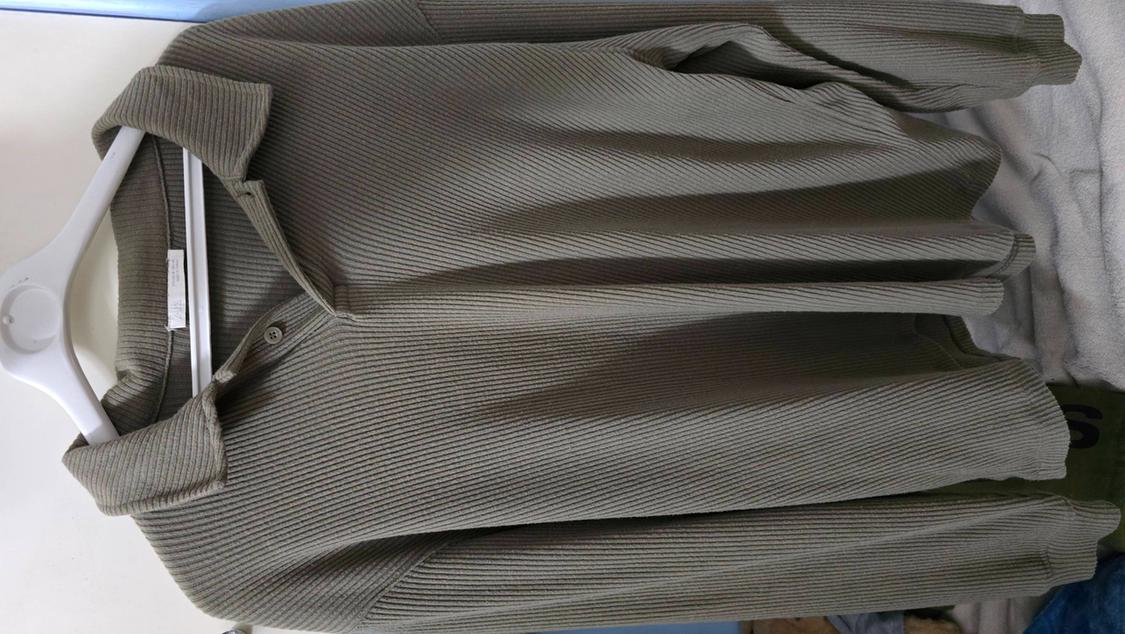 Ribbed khaki knit shirt hanging on a white hanger against a light surface.