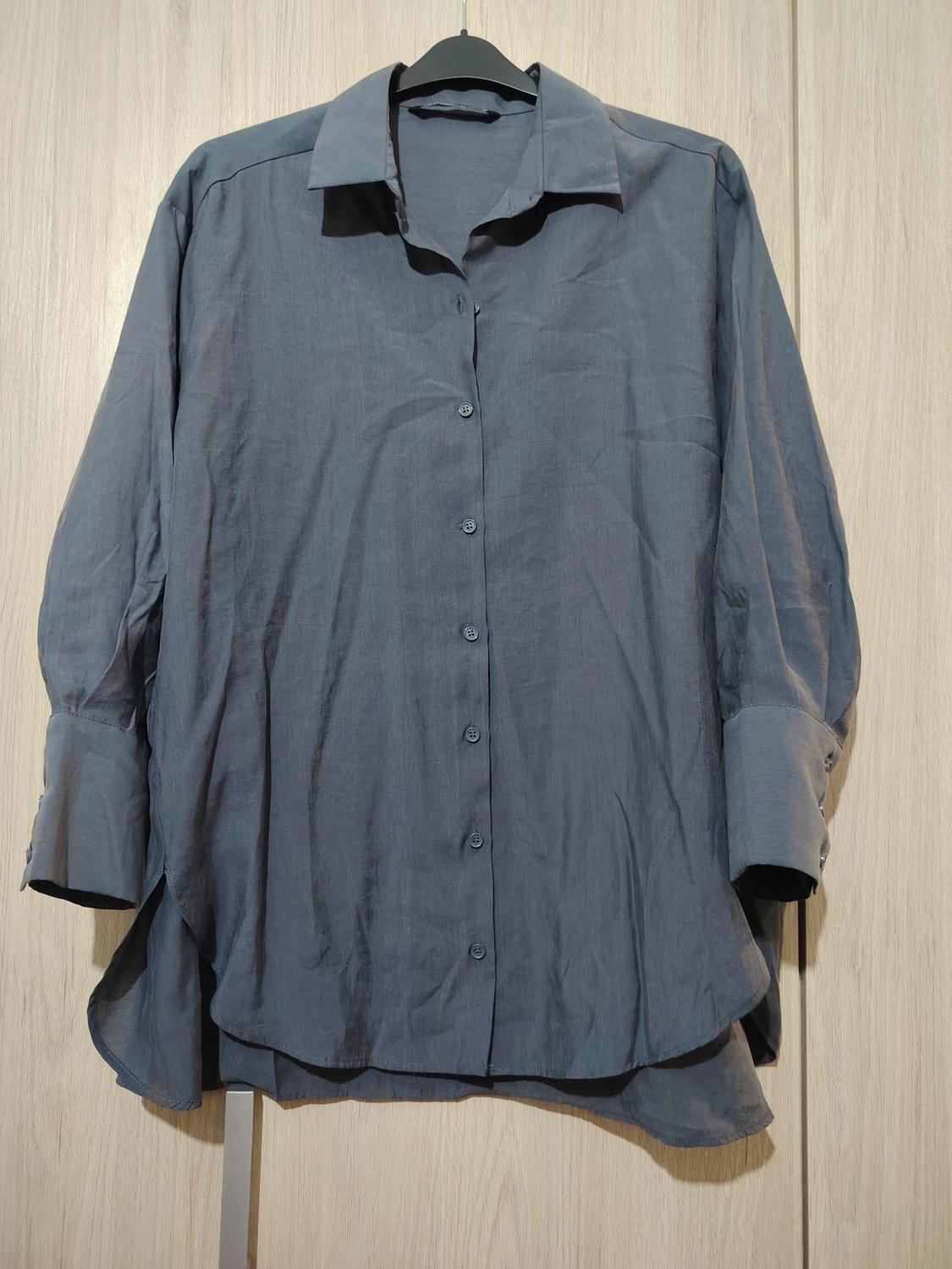 Blue long-sleeved shirt hanging on a black hanger against a light wooden background.