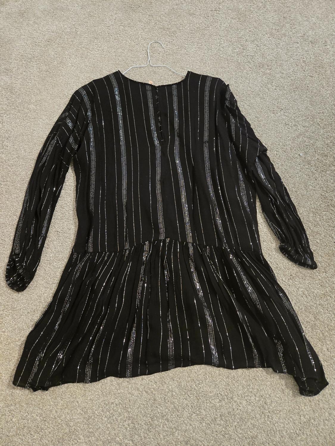 Back view of a black dress with shiny vertical stripes and long sleeves.