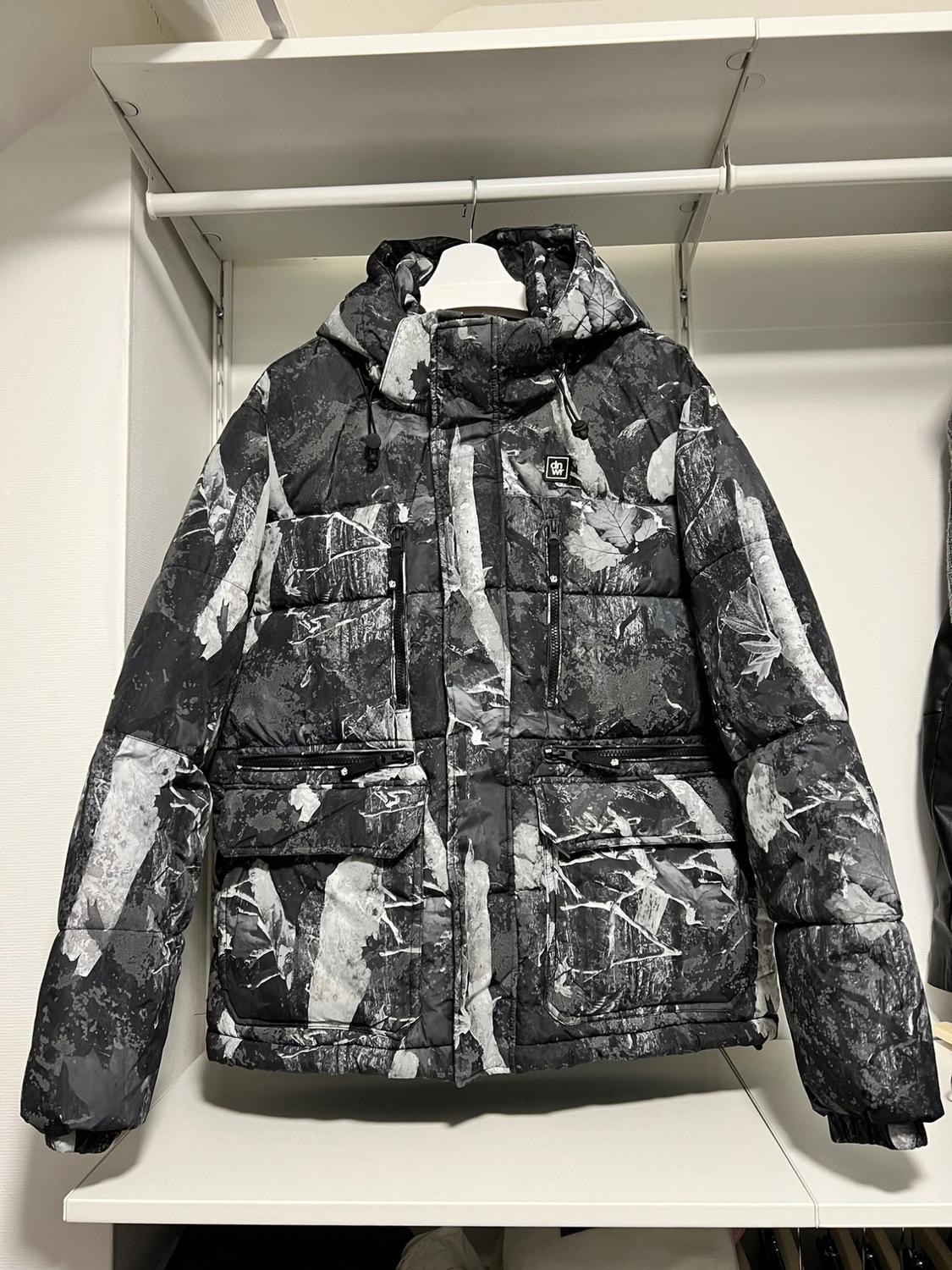 Black and white hooded padded jacket with an abstract print, hanging on a white hanger in an open wardrobe.
