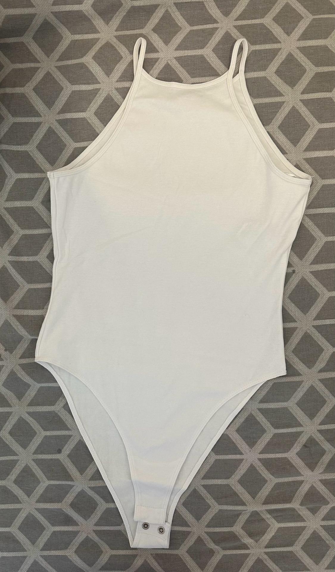 White thin-strap bodysuit with snap button fastening, set against a grey geometric patterned background. Flat lay, casual composition.
