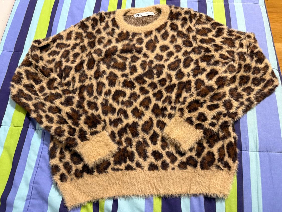 Leopard print fleece jumper on a blue, green, and purple striped quilt. Visible label on the collar.