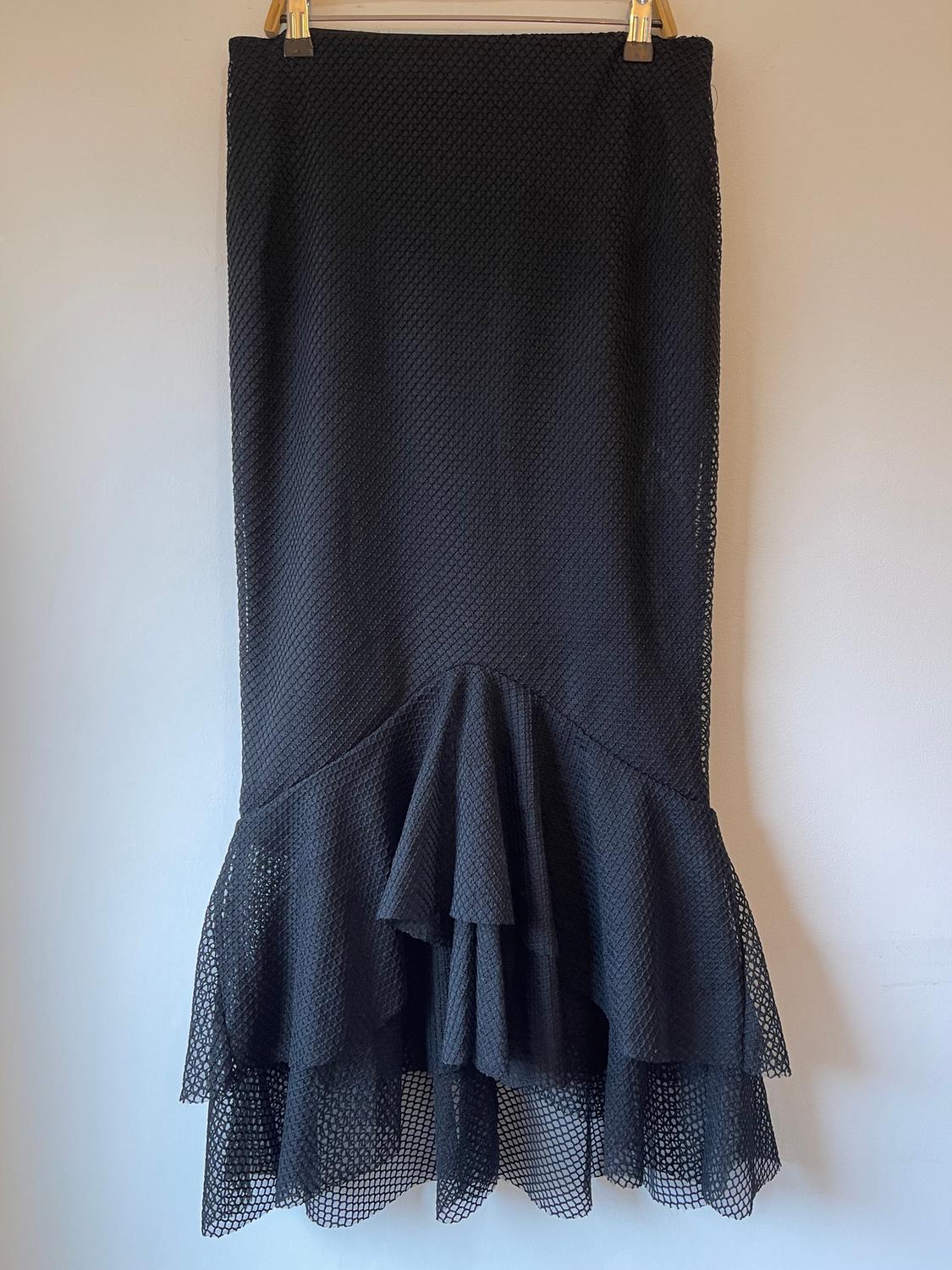 Black mesh skirt with ruffled hem, hanging on a hanger against a white background.