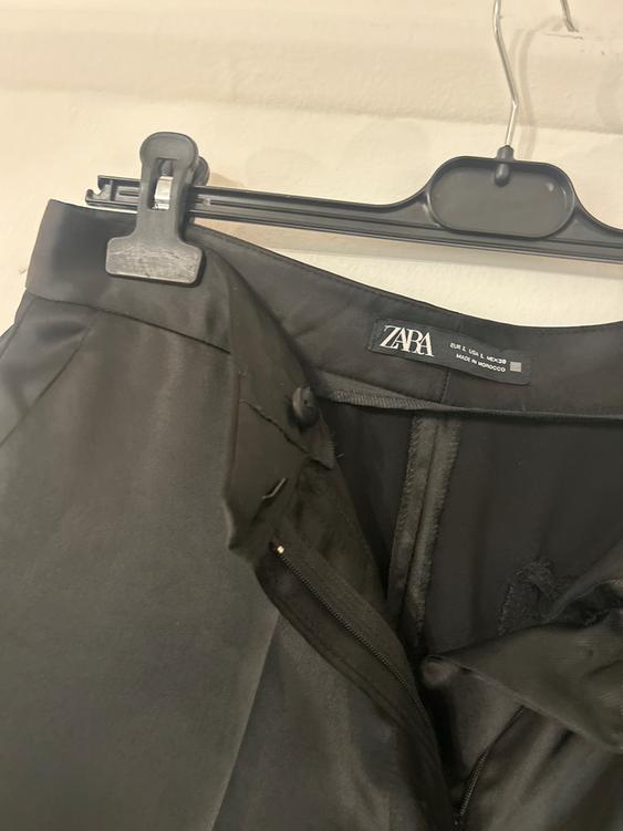 Black satin trousers hanging on a black hanger. Visible label with the ZARA brand and "Made in Morocco". Zip open.