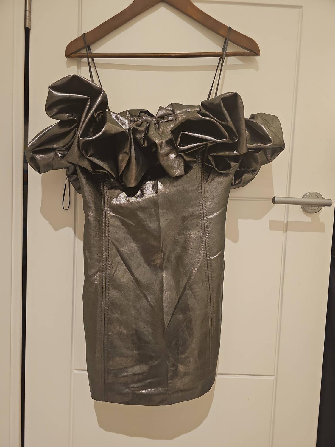 Metallic short dress with thin straps and a frilled neckline, hanging on a wooden hanger over a white door.
