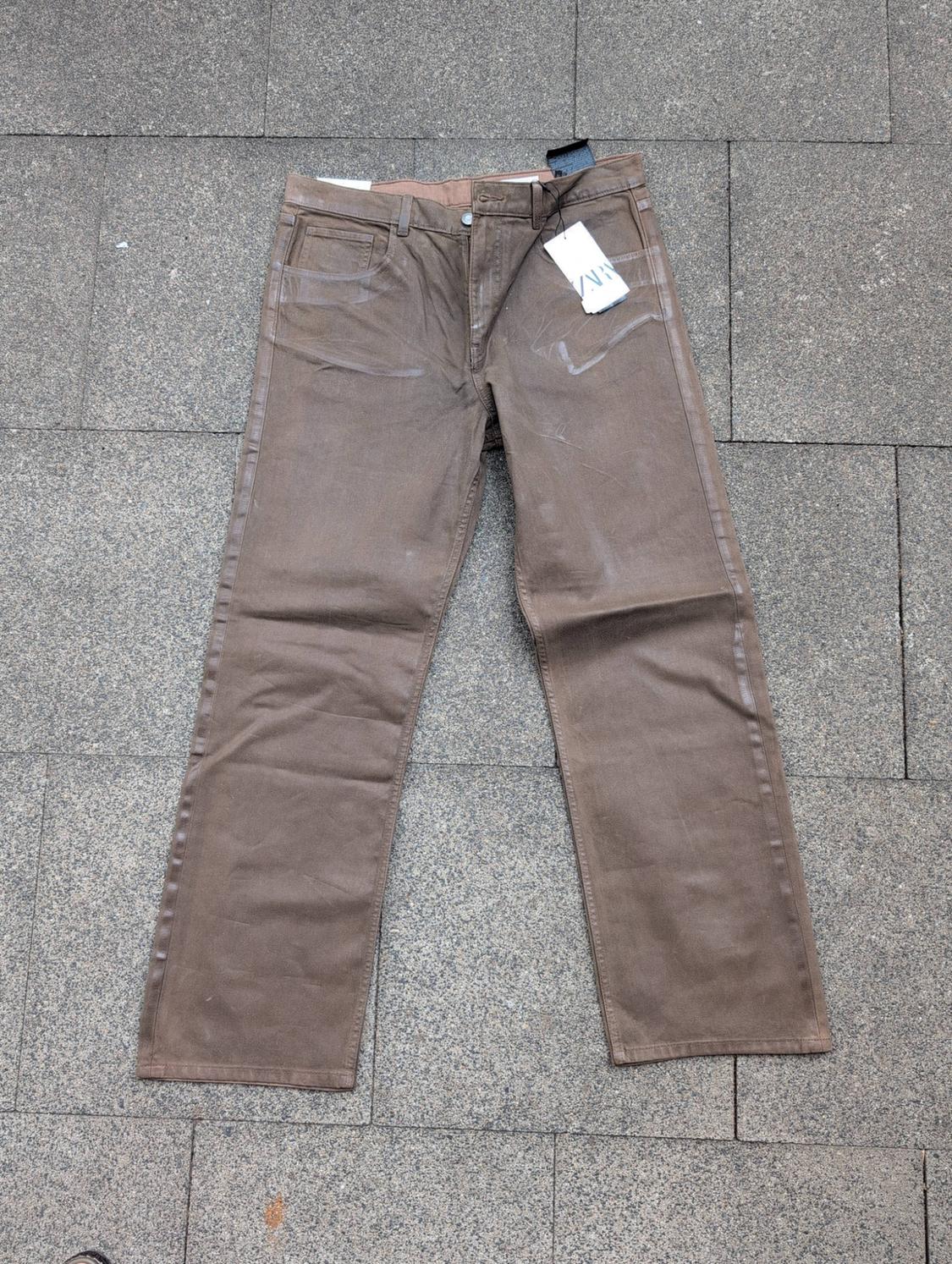 Brown trousers laid out on a grey tiled floor. Label with the text ZARA.