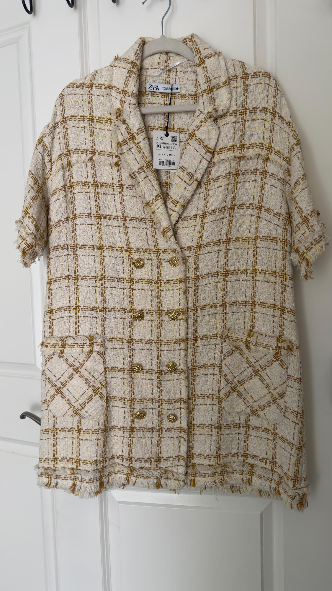Beige and gold plaid jacket hanging on a hanger. Detail of gold buttons and visible Zara tag.