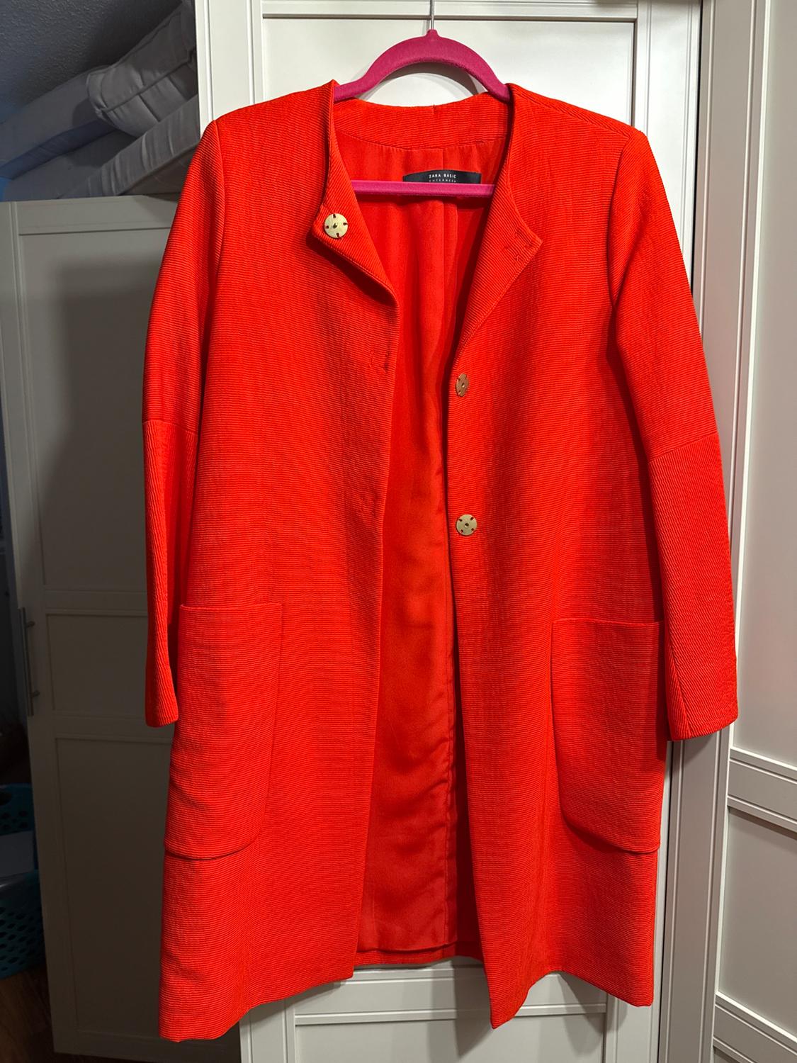 Red coat hanging on a pink hanger, with decorative buttons and large pockets, against a white closet background.