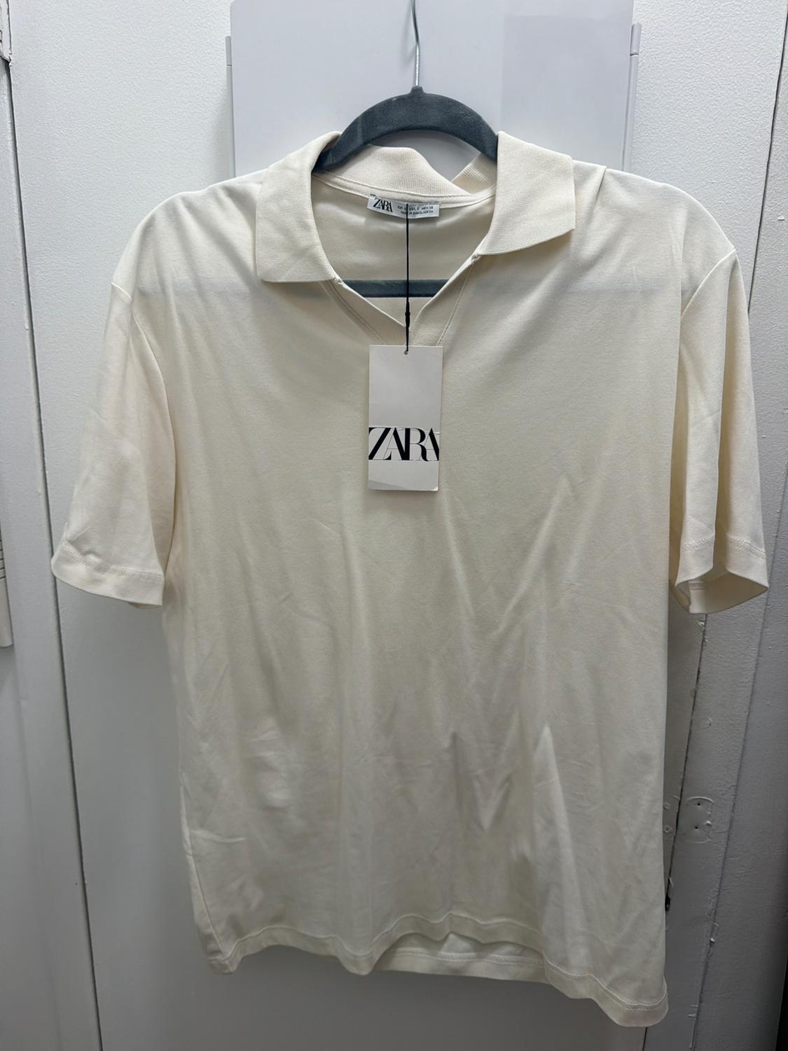 Cream-colored short-sleeve polo shirt hanging on a black hanger. White background. Visible label with the text ZARA.
