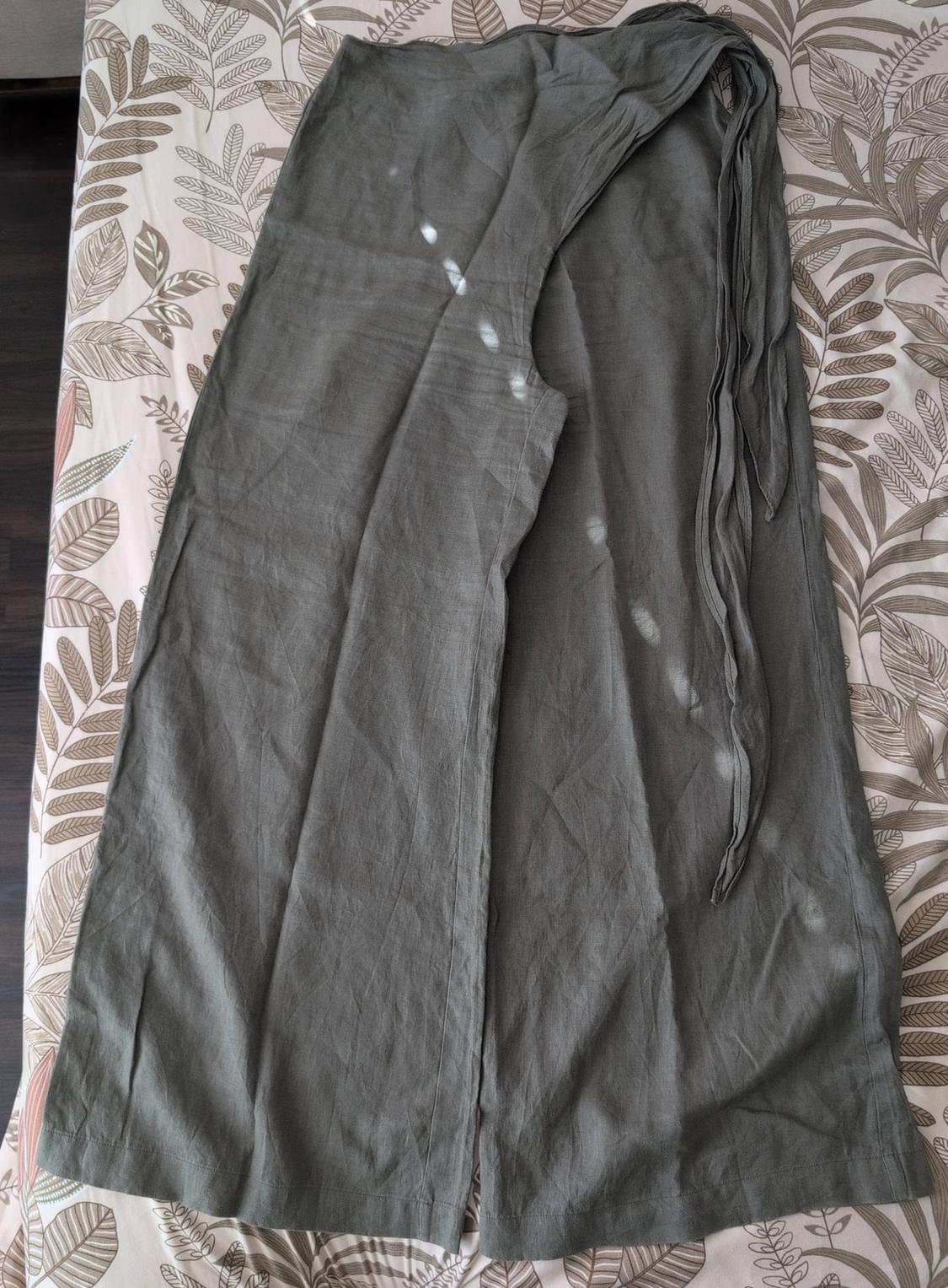 Olive green wide-leg pants with a tie waist, resting on a leaf-print sheet under natural light and soft shadows.