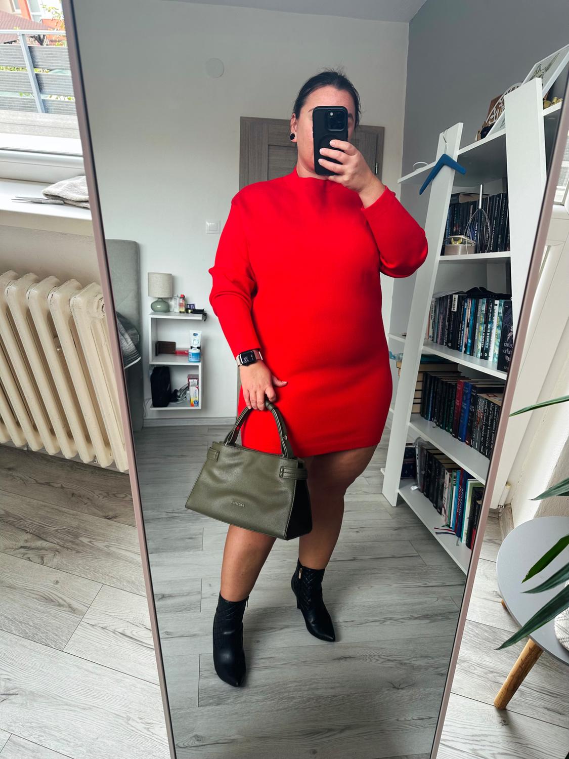 Γυναίκα που κάνει selfie στον καθρέφτη του δωματίου της. Φορά ένα κόκκινο κοντό φόρεμα με ψηλό ντεκολτέ, μαύρα μποτάκια και πράσινο λαδί τσάντα.