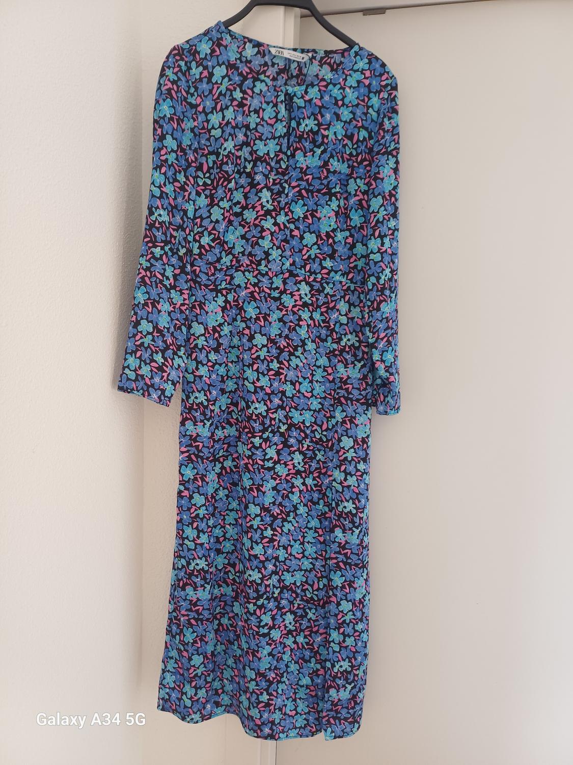 Long-sleeved dress with a floral print in blue and pink tones, hanging on a hanger. Visible text: "Galaxy A34 5G".