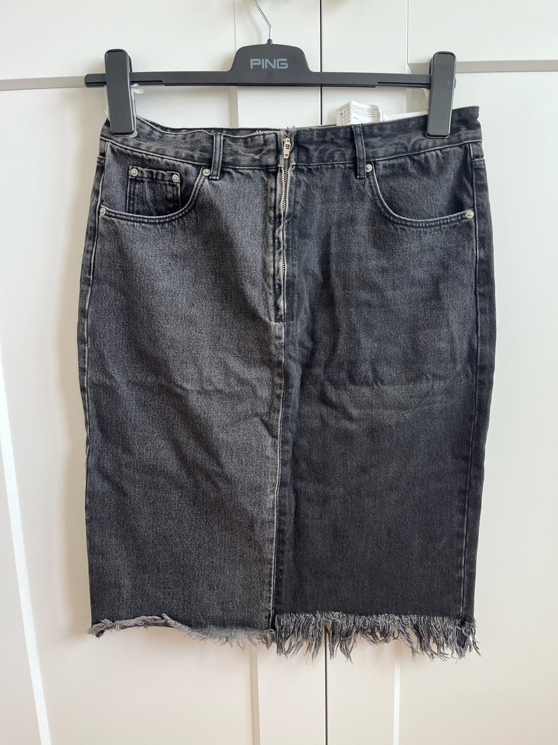 Dark grey denim skirt with a frayed hem and zip, hanging on a black hanger with the text PING on a white background.