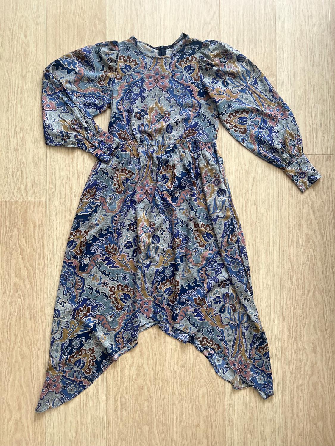 Floral and geometric print dress in shades of blue, pink, and brown, on a light wooden floor.