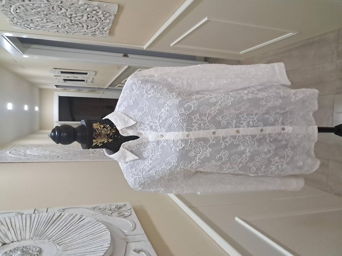 Mannequin in a white floral lace shirt in a corridor decorated with artistic wall panels.