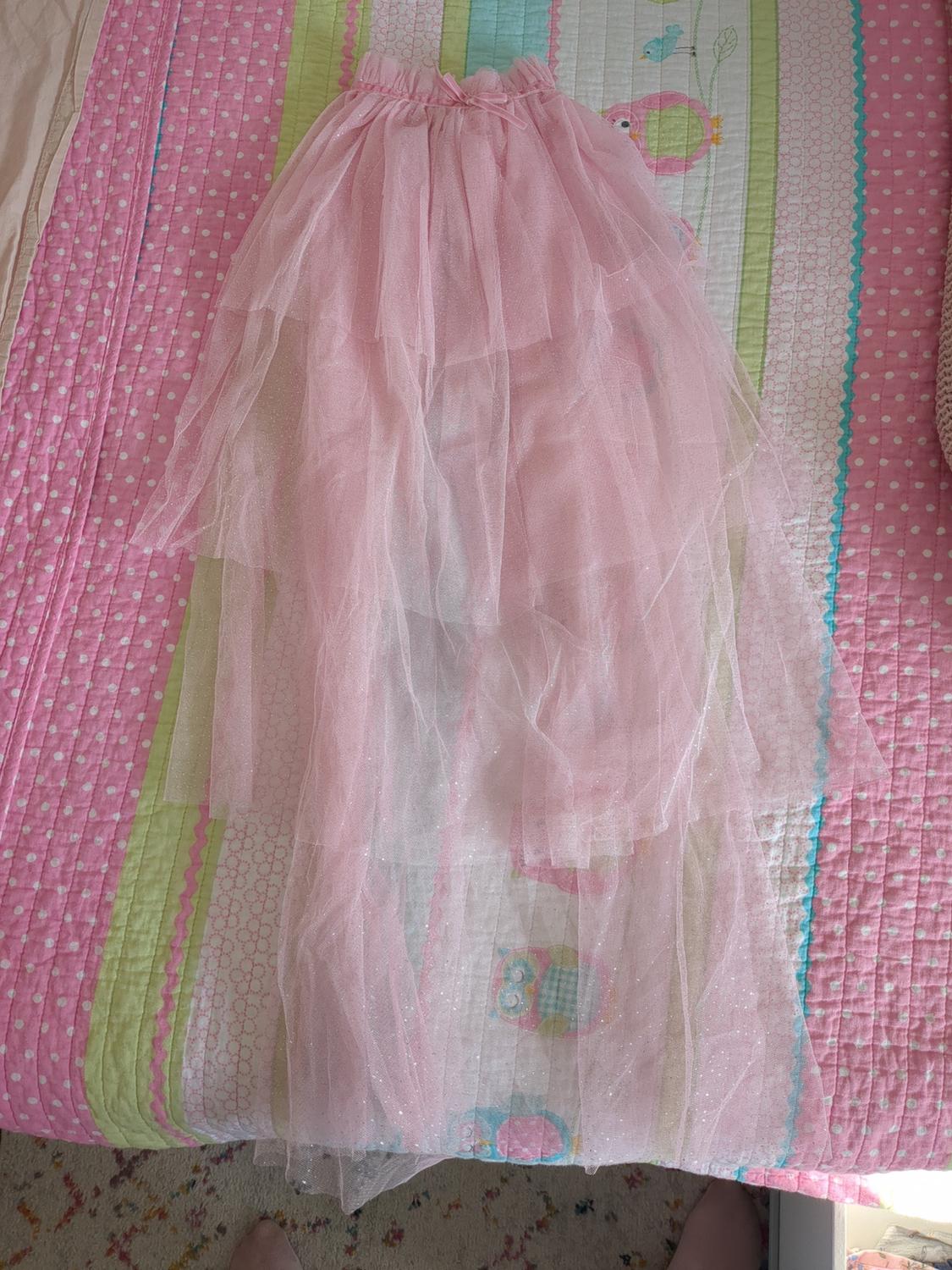 Light pink tulle skirt on a colorful bedspread with owl and bird patterns. Polka dot and striped background.
