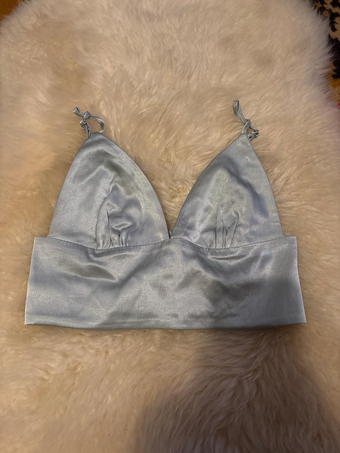 Light grey satin bra with thin straps on a beige faux fur rug.