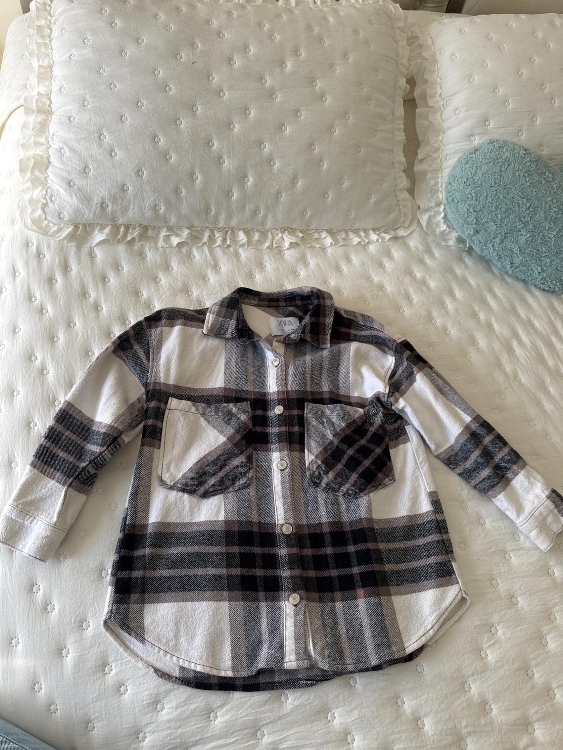 Brown and white checked shirt on a bed with white quilts and a blue cushion.