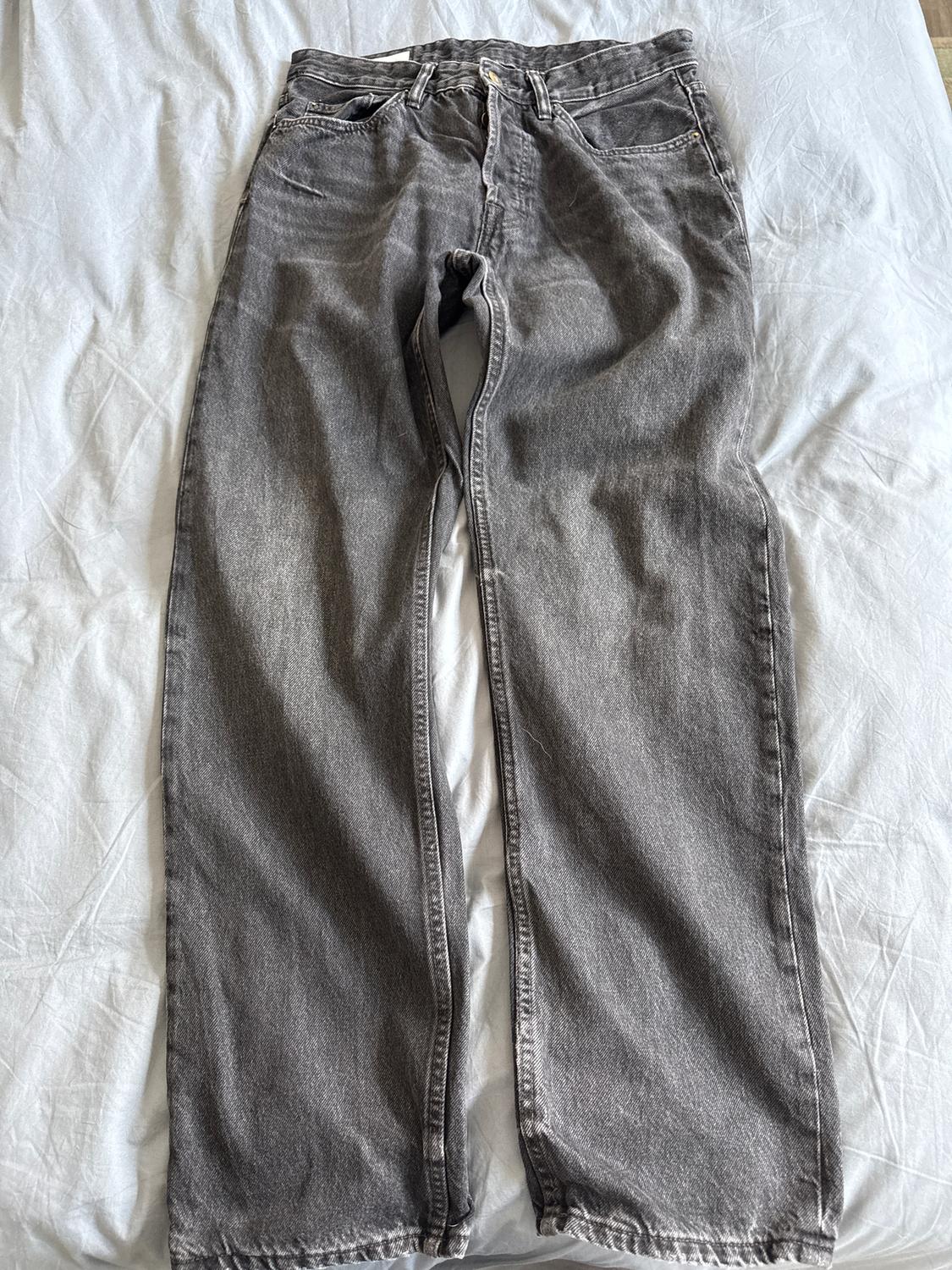 Grey straight-cut denim jeans laid flat on a white surface, showcasing stitching details and pockets.