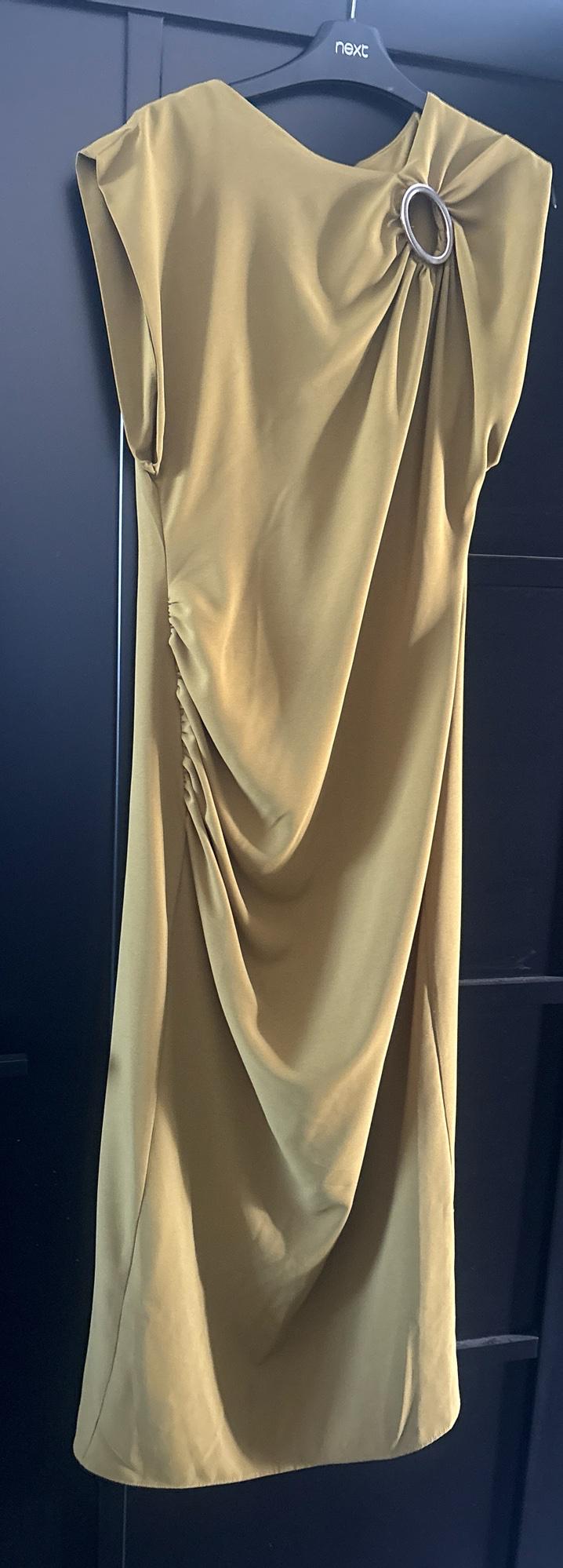 Mustard dress with side draping and a silver-tone ring, hanging on a hanger with the text next against a dark background.