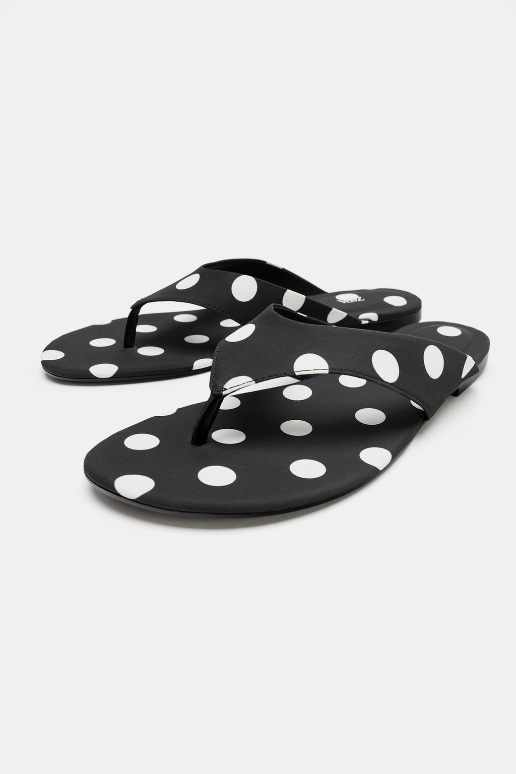 Front view of black flat thong sandals with a white polka dot print and wide straps.