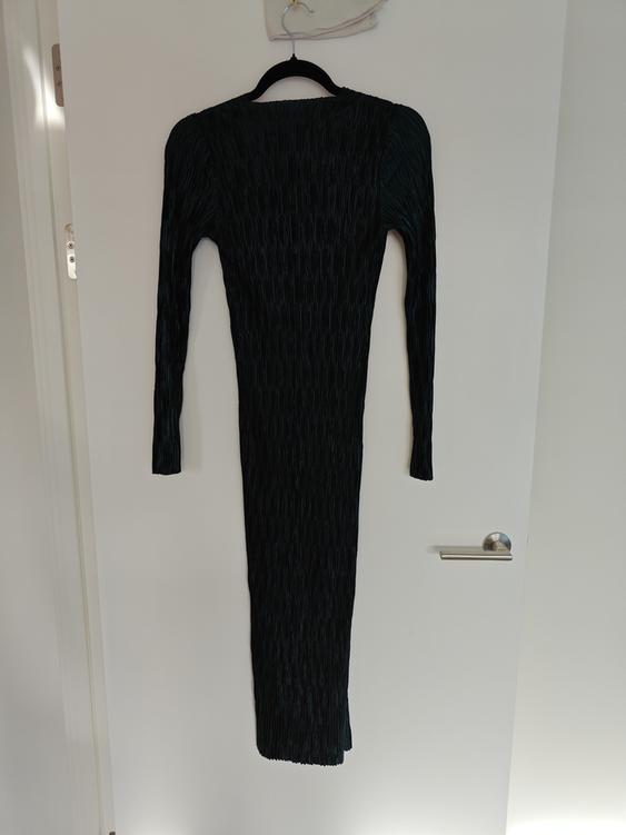 Black long-sleeved dress with a pleated texture, hanging on a black hanger over a white door.