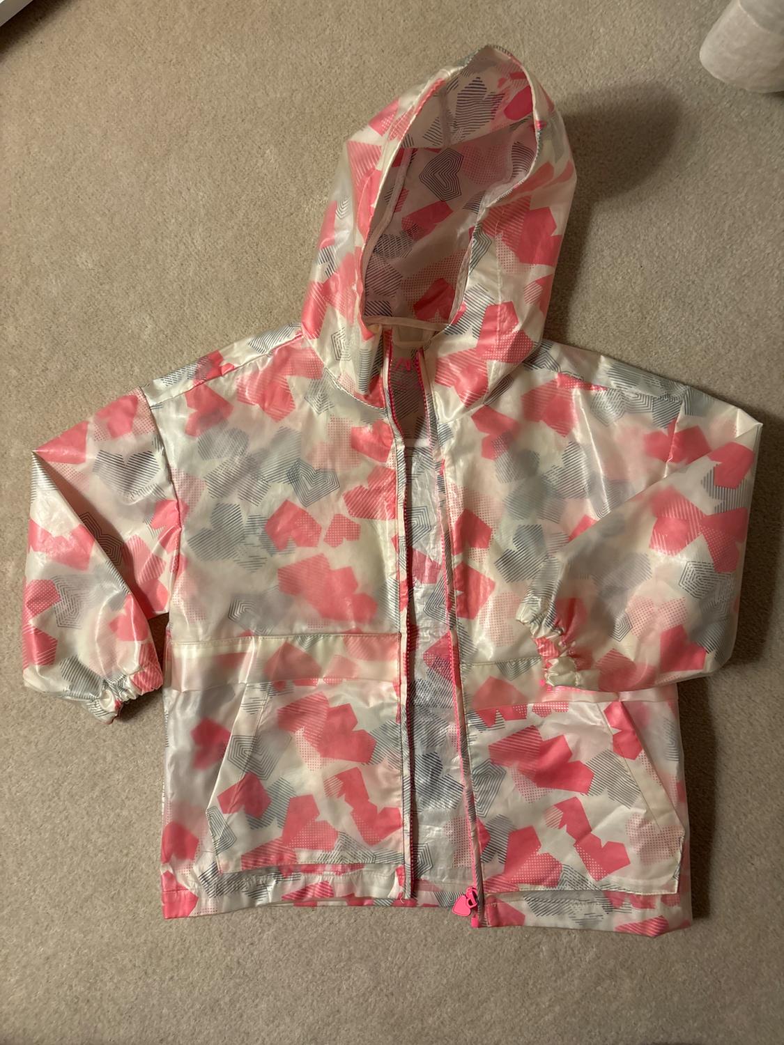 Pink, grey, and white hooded jacket with a geometric pattern on a beige rug.