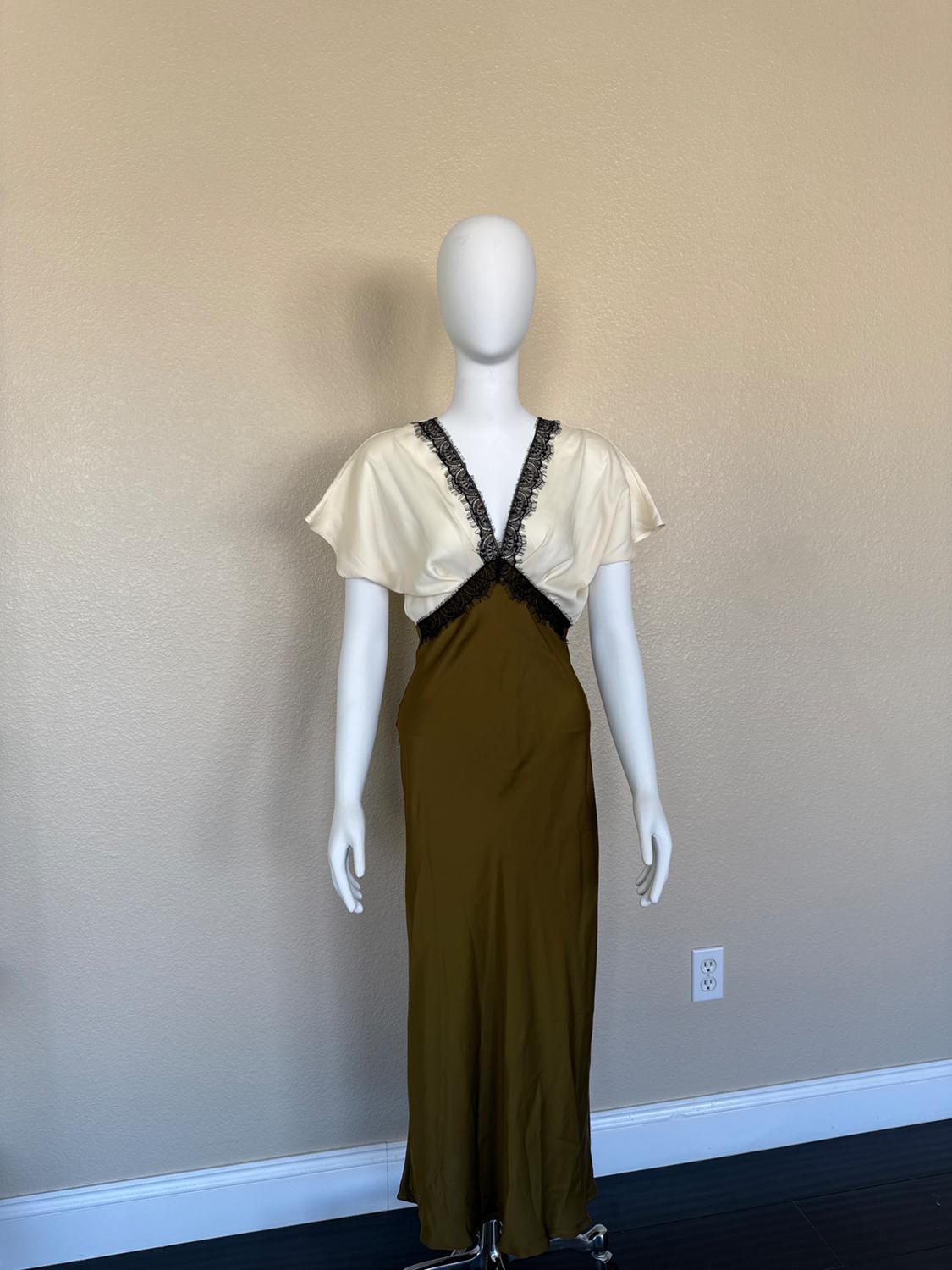 Mannequin with long satin dress, cream top with black lace, and brown skirt. Beige wall background.