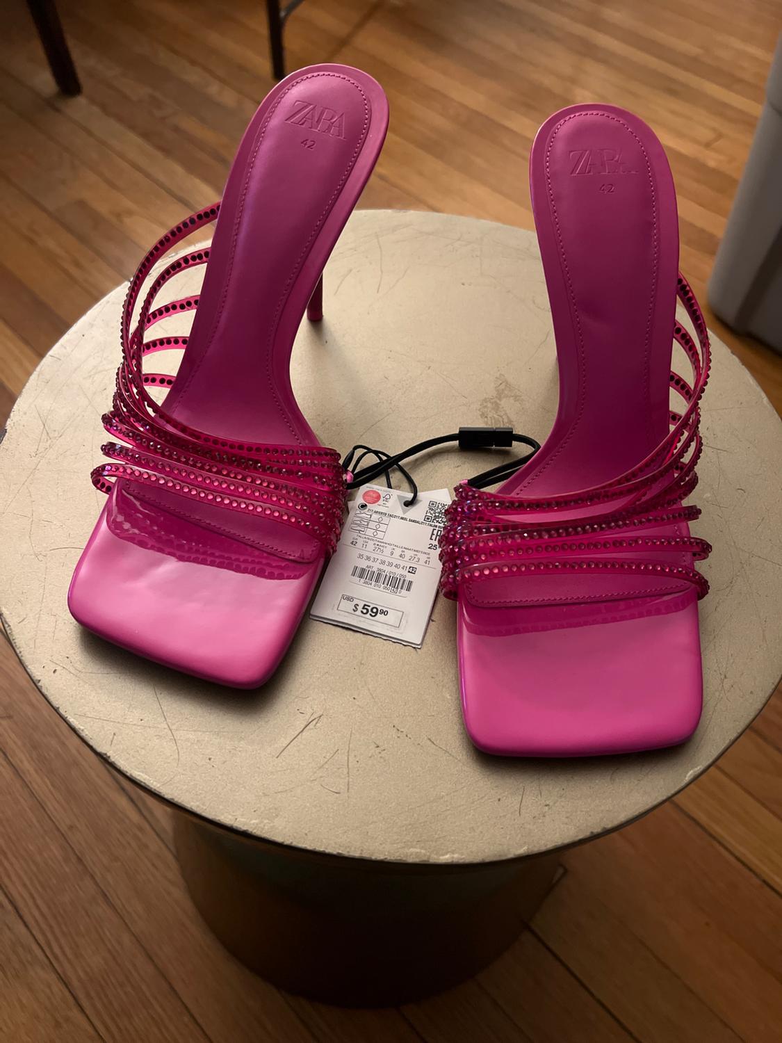 Fuchsia high-heeled sandals with decorative straps on a round table. Visible tag with price of $59.90.