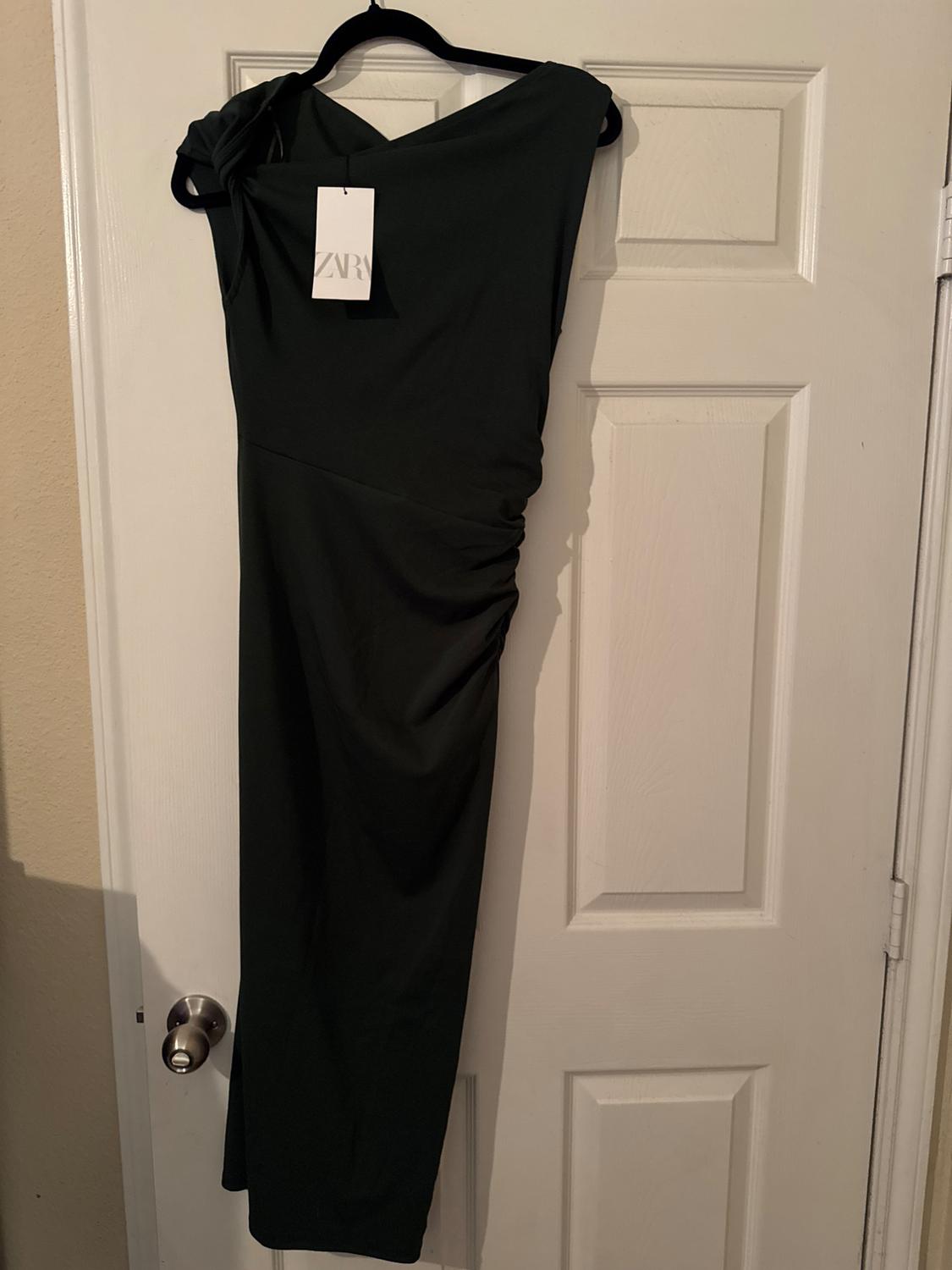 Black dress hanging on a white door, with visible tag. Asymmetrical design and draped on the shoulder.