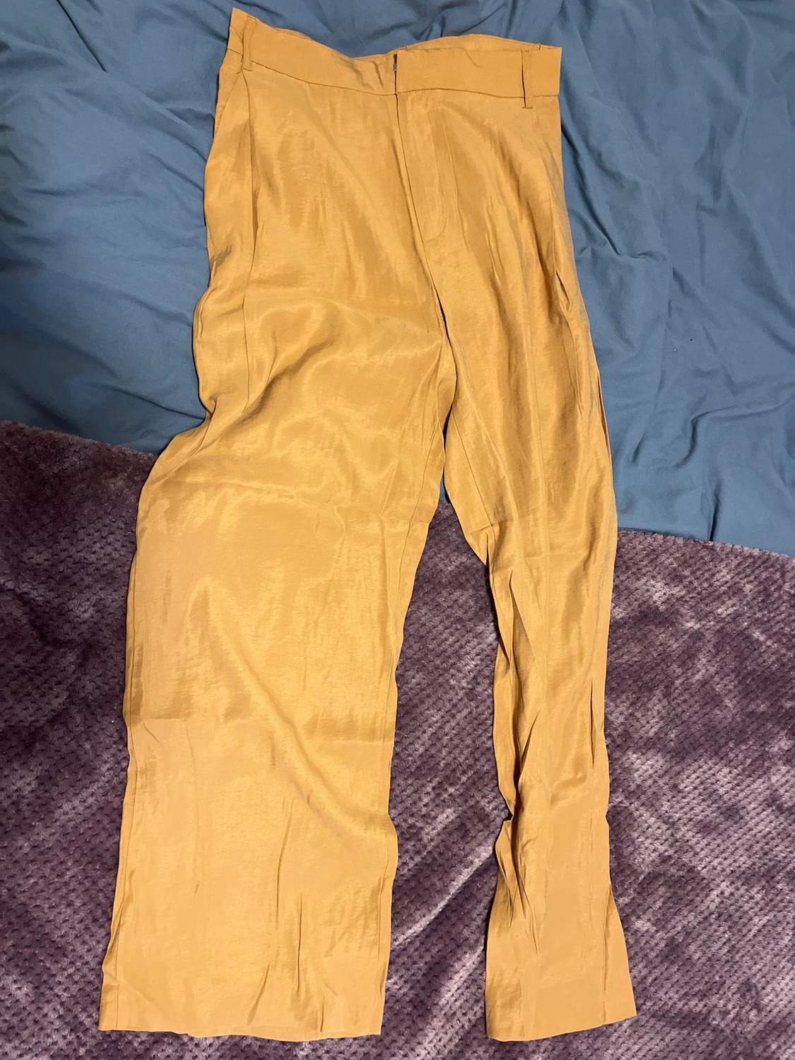Yellow trousers laid out on a bed with blue sheets and a purple bedspread. Soft, lightweight fabric, with no visible patterns.