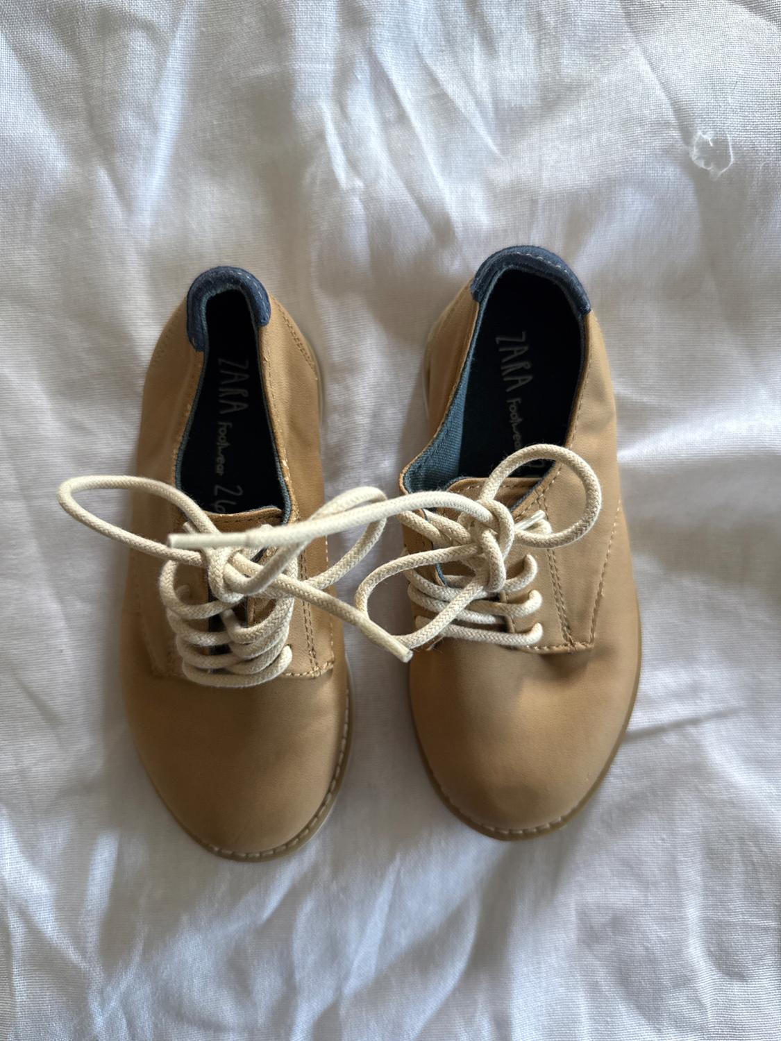 Beige shoes with white laces on white fabric. Dark blue interior with "ZARA footwear" text visible on the insoles.