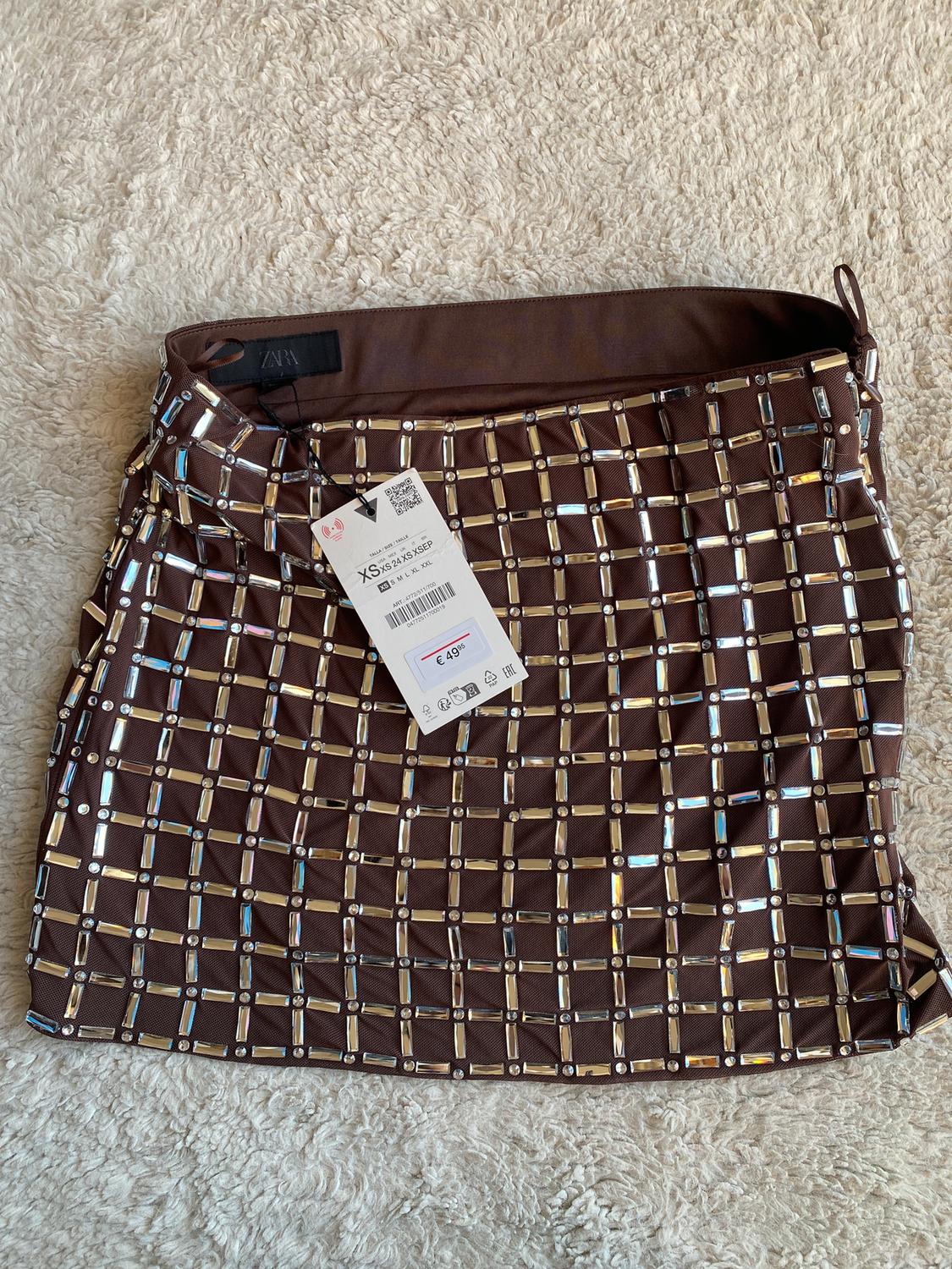 Brown skirt with square metallic details on a beige rug. Visible tag with price of £49.95. ZARA brand.