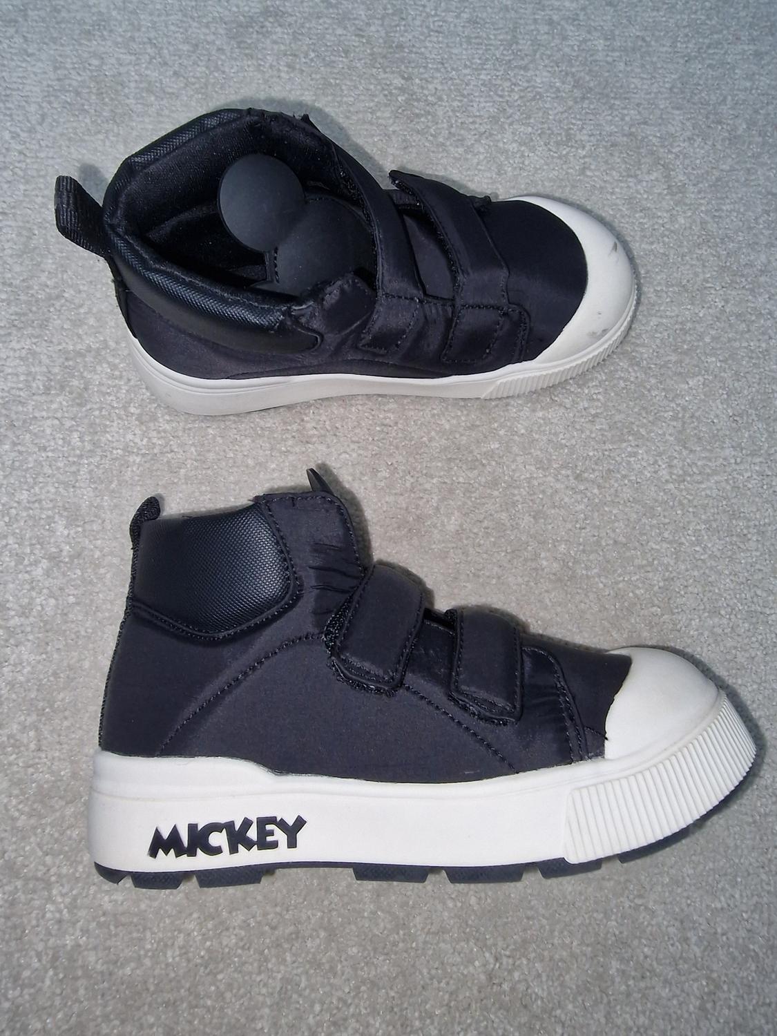 Black high-top trainers with white soles and touch-and-close fastening, Mickey Mouse design on the side, on a grey carpet.