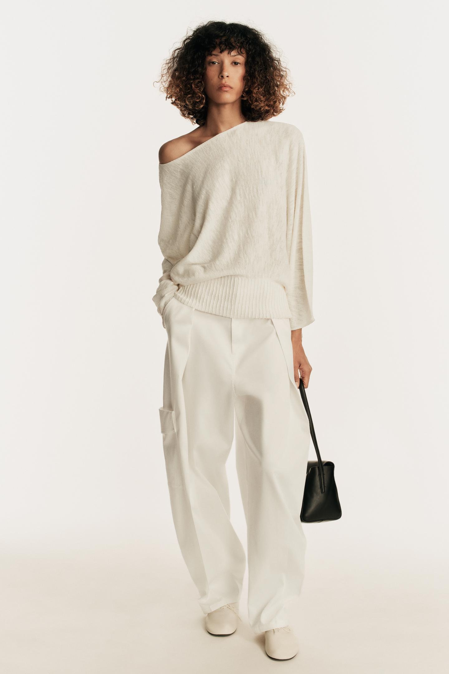 Cream boat-neck sweater set with long sleeves and a fitted hem, wide-leg white pants with side pockets, and a black handbag.