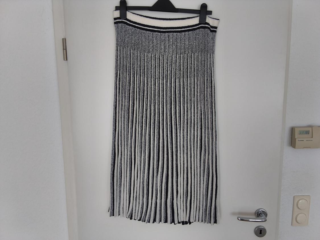 Black and white pleated skirt hanging on a hanger over a white door. Minimalist background with light switch and thermostat.