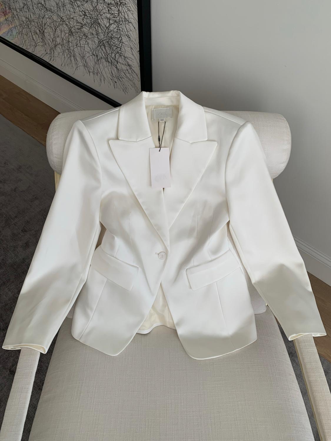 White satin Americana with a label, placed on a light fabric chair. In the background, a black-and-white abstract painting.
